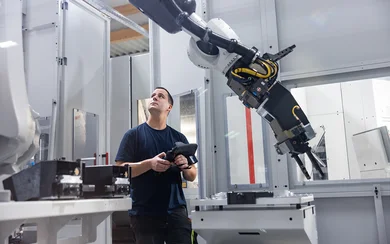 Ein Mitarbeiter im Fräsen schaut zu einem Roboterarm hoch und hält benutzt die Bedienung dazu
