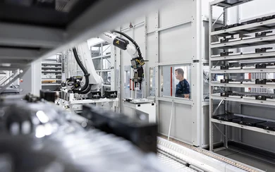 Ein Mitarbeiter im Fräsen beobachtet durch die Scheibe einer Linearanlage, den Roboterarm, der an mehrere Fräsmaschinen angeschlossen ist