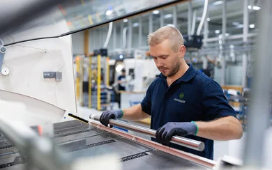 Ein Mitarbeiter im Drehen legt eine Materialstange in einen Stangenlader, der an die Drehmaschine angebunden ist